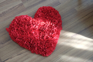 Heart shape doormat, in top view, red color, on wood floor with natural sunlight