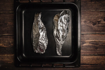 Fish wrapped in foil on a baking sheet and on a wooden table. Cooking fish in the oven.