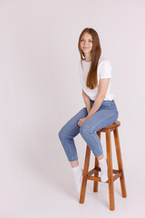 girl in a white T-shirt and blue jeans on a chair on an isolated background