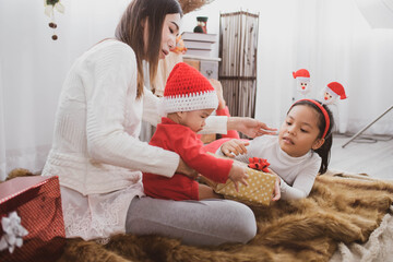 parent and two little children having fun and playing together near christmas tree indoors. merry christmas and happy holidays. cheerful mom and her cute daughters girls exchanging gifts.