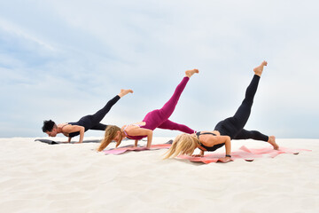 Three beautiful slender young women perform yoga exercises on the beach