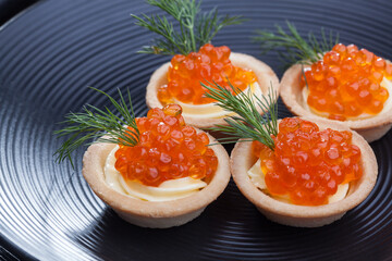 tartlets with butter and red caviar and dill on the black plate . Delicious snack