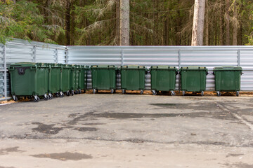 Green garbage cans stand on the paved area.