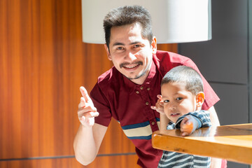 Smiling father playing with baby son at home. Asian Father and son wearing casual shirt was smiling together with happiness, happy family relationship concept.