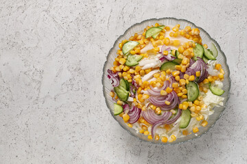 Vegetable salad with peking cabbage, sweet corn kernels, sliced onion and cucumber in a deep bowl on a concrete background, top view. Concept of healthy and vegan food.