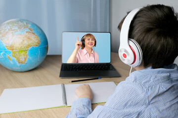 schoolchild, kid 7-8 years old doing homework in front of a laptop, the teacher on the screen leads...