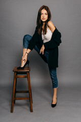 Amazing brunette with long hair in jacket and jeans put her foot on the back of a chair