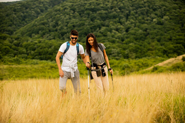 Fototapeta na wymiar Smiling couple walking with backpacks over green hills