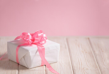 Beautiful white box with pink ribbon on the light wooden table with copy space for text