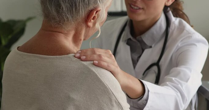Close up nurse hand on older female patient shoulder during talk at hospital. Medical gp therapist worker in white coat give professional advice, assistance to senior clinic client. Healthcare concept