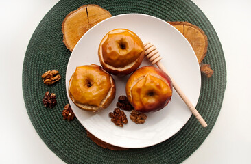 Baked apples stuffed with nuts, raisins and honey in a plate on a white plate. Green plate holder.