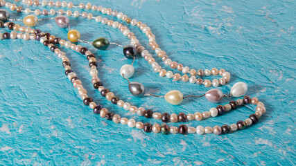 Different long natural  multicolored  pearl beads are nicely laid out on a blue textured surface.  