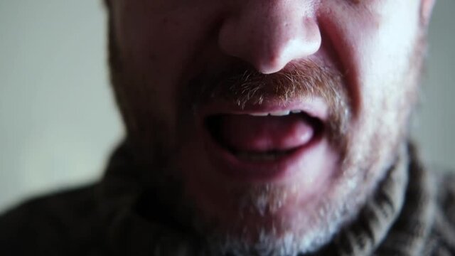 An unshaven man speaks aggressively in close-up.