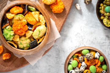Various Japanese snacks in a wooden bowl close-up. Rice crackers with wasabi and nori, peanuts with...