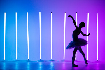 Portrait of a young ballerina on pointe shoes in a white tutu against background of bright neon...