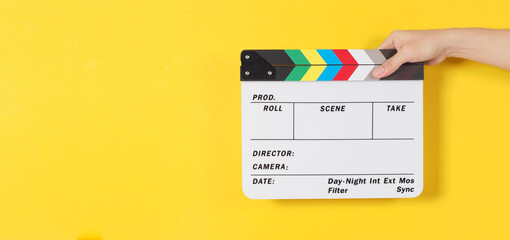 Hand is holding clapperboard or movie slate or slate or clapper board .It is used in video production and cinema ,movies industry on yellow background © nisara
