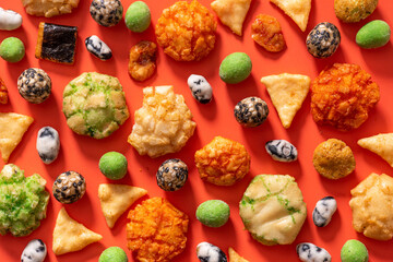 Pattern from various Japanese snacks on a red background. Top view, flat lay. Rice crackers with wasabi and nori, peanuts with sesame seeds, and other snacks. Mix traditional Japanese snack food.