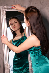 sexy attractive brunette woman in elegant green aquamarine dress in front of a mirror. beautiful sensual girl