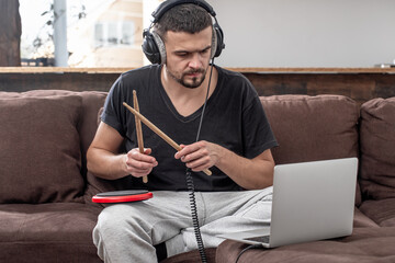 A young man with headphones learns to play the drum using online lessons.