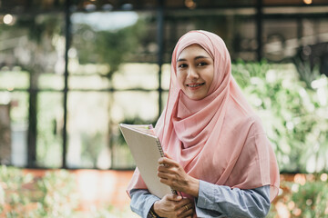 Smiling Muslim girl student standing and holding a book at campus