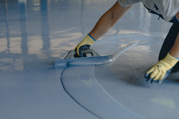Fototapeta na wymiar The worker applies gray epoxy resin to the new floor