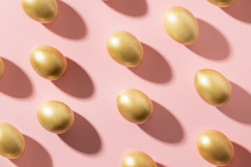 Easter golden eggs with sunny shadow on pink background. View from above. Flat lay.