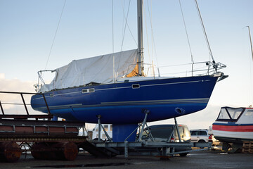 Blue sloop rigged yacht standing on land in a small harbor on a clear winter day. Waiting for the...