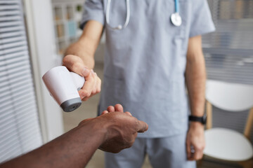 Close up of male doctor pointing infrared thermometer at patients hands during temperature check in hospital, copy space