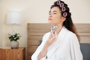 Beautiful young Asian woman massaging neck with metal roller to get rid of wrinkles