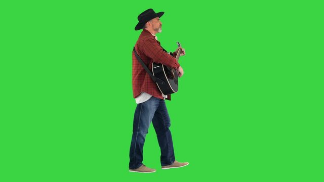 Man in a cowboy hat singing and playing the guitar while walking on a Green Screen, Chroma Key.