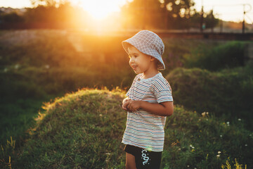 Charming boy with blue hat is posing in a green field smiling in the sunshine © Strelciuc