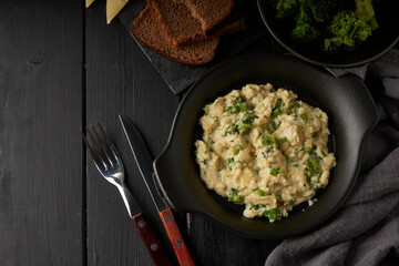 Scrambled eggs with broccoli and green onion served in dark plate with bread on table