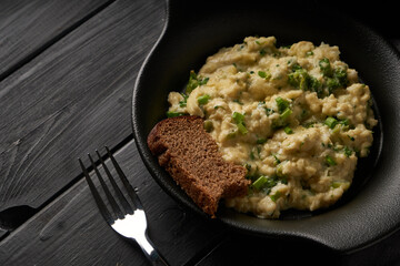 Scrambled eggs with broccoli and green onion served in dark plate with bread on table