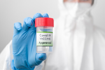 Approved Covid 19 vaccine bottle in doctors hand. Doctor in protective suit, face mask, safety googles and rubber gloves demonstrate vaccine against coronavirus. 