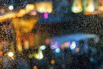 City lights of the night during the rain behind a glass covered with drops of water.
