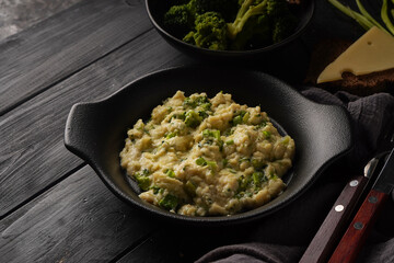 Scrambled eggs with broccoli and green onion served in dark plate with bread on table