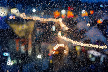 City lights of the night during the rain behind a glass covered with drops of water.