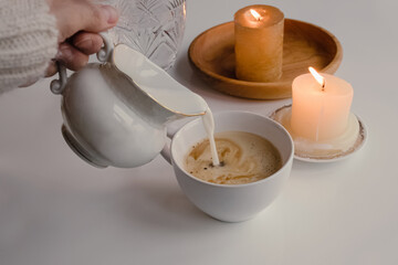 Feminine hand pouring milk from vintage style milk jug into cup of coffee