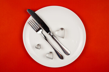 A white plate with a knife and fork on a bright red background.Baking dish. Studio photo. Valentine's Day. The view from the top.