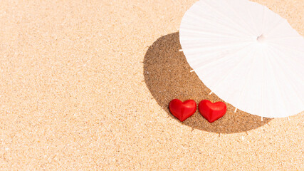 Valentine day concept. Two red hearts - symbol of love couple on sand paradise tropical beach under parasol. Love, togetherness, marriage. Traveling together. Banner. Copy space