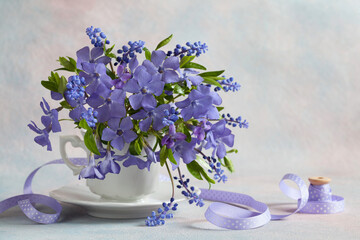 A bouquet of blue flowers of periwinkle, muscari and violets in a cup on a decorative background....