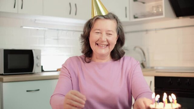 Cheerful Mature Woman Talking To Family By Video Application Blowing Out Candles