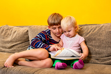 The older brother is teaching his sister English while sitting on the couch.