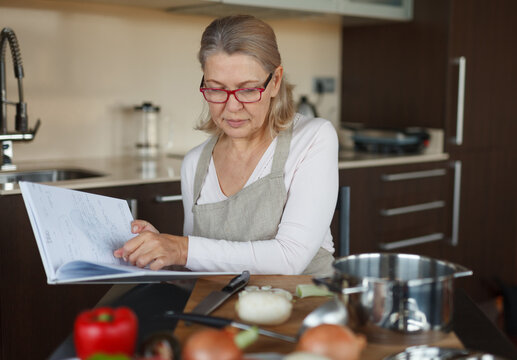 An outdated concept - recipes in a notebook. Aged woman in the kitchen.