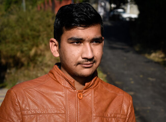 Fototapeta premium picture of indian boy looking away from camera wearing leather coat and standing outdoor