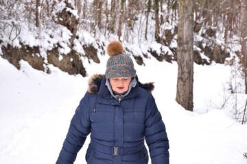 Retired woman in jacket and hat with bright colors looking where she steps on a snow-filled path in the forest. Scene after the snowstorm called Filomena in Spain. January 2021.