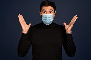 Shocked young business man in black sweater and sterile face mask isolated on Pacific Blue...