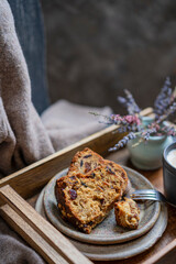 Fototapeta na wymiar A piece of a sponge or bundt cake with dried fruits on a wooden tray with lavender flowers on a rustic chair. Beautiful desert or breakfast, copy space. Homemade freshly baked pie.