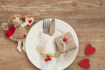 Festive table setting for Valentine's Day with gift boxes, plate, fork, knife and hearts on a wooden table. Love consept.