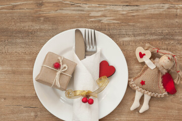 Festive table setting for Valentine's Day with gift boxes, plate, fork, knife and hearts on a wooden table. Love consept.